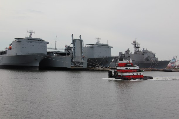 Red tug in front of three ships at a private shipyard.
