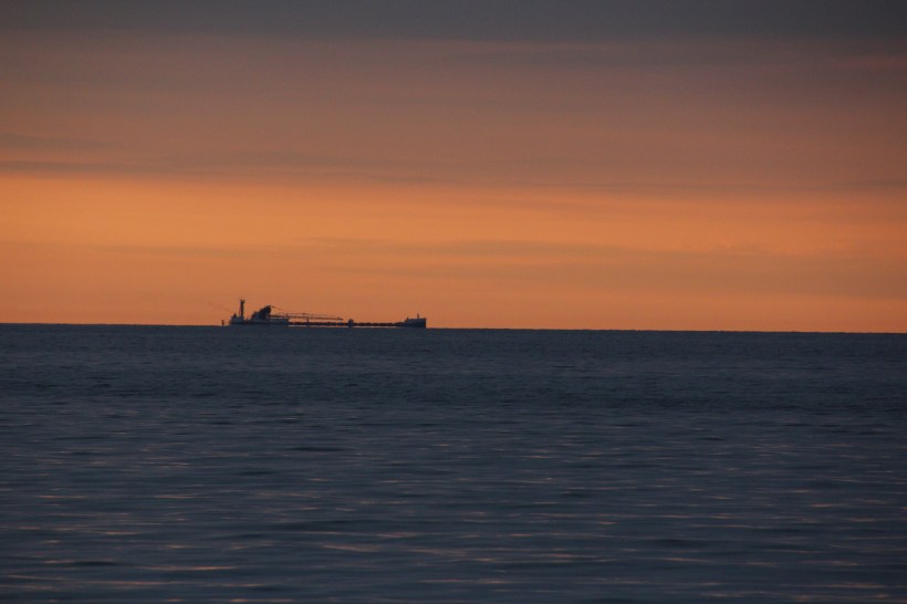 Fishing boat chugging along the horizon at sunrise.